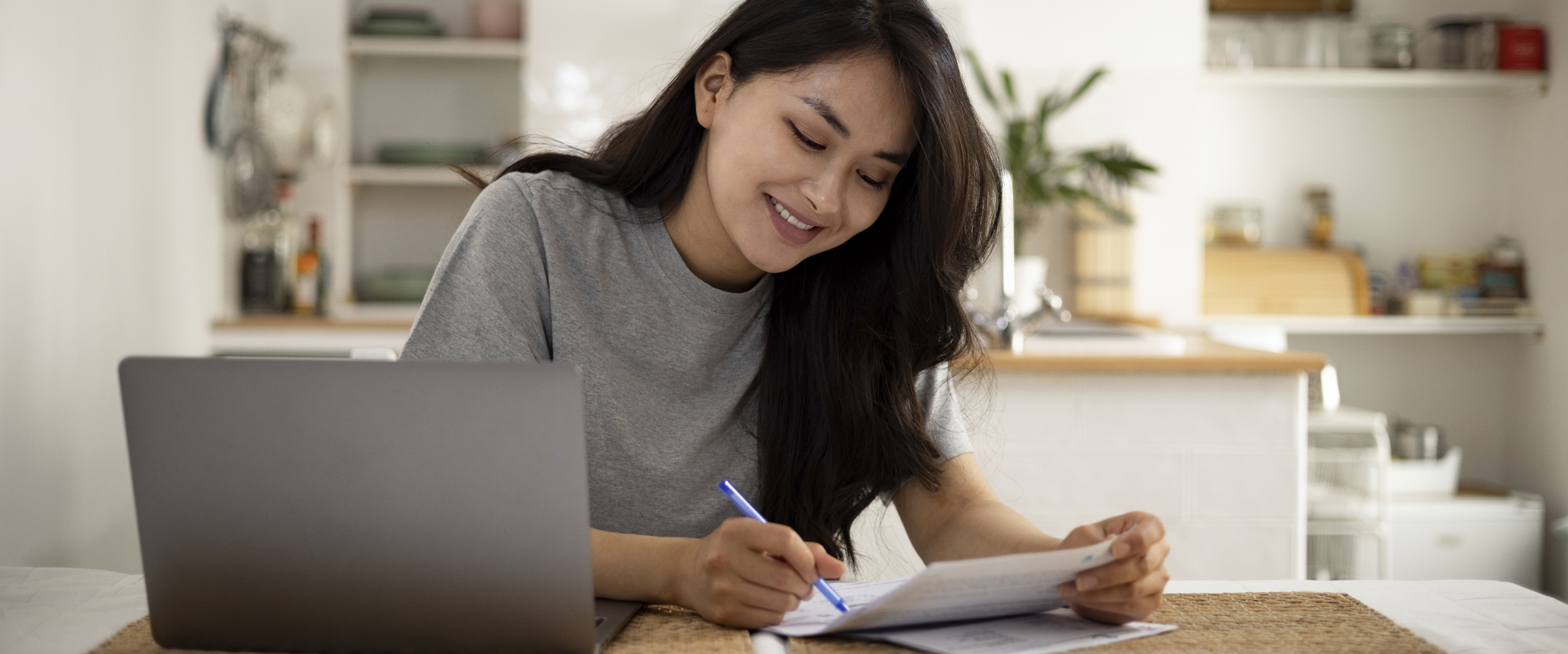 Girl on computer looking at paper on desk.